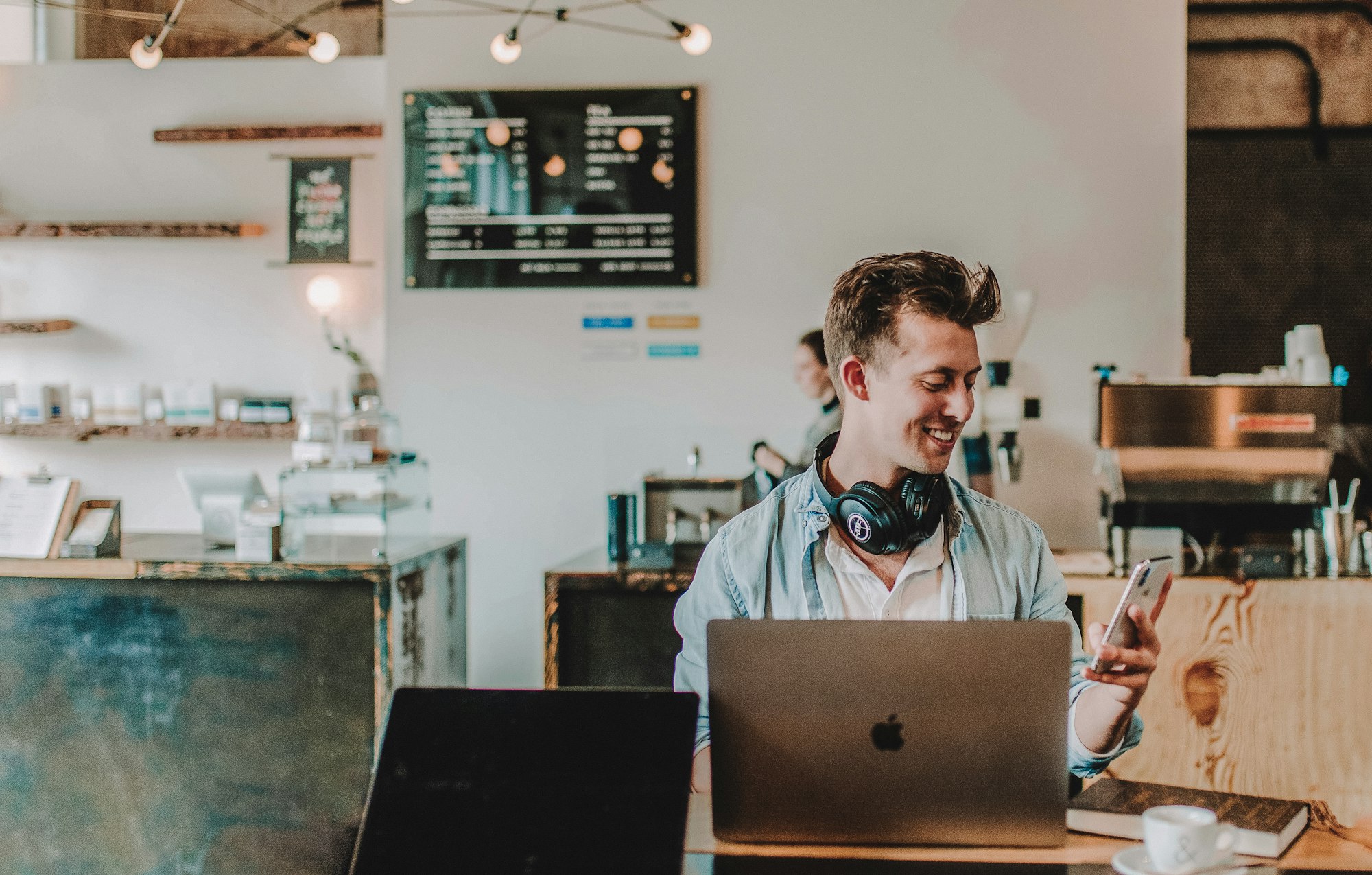 Male at a coffee shop smiling at the phone while working on the computer. 