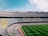 A large, empty football stadium with rows of seats in the stands. The seats form a pattern with the words 'MES QUE UN CLUB' visible. The grass on the field is neatly maintained with alternating light and dark green stripes.