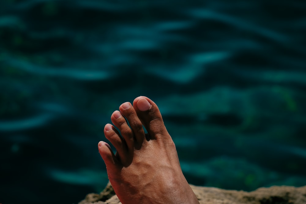 a person's foot resting on a rock by the water
