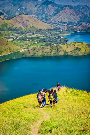 Teenagers hiking through lush green hills with backpacks and bright smiles.