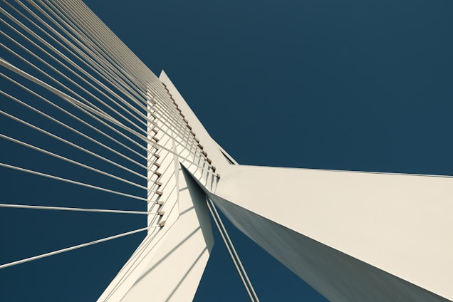 A panoramic view of a massive cable-stayed bridge under construction against a clear blue sky.