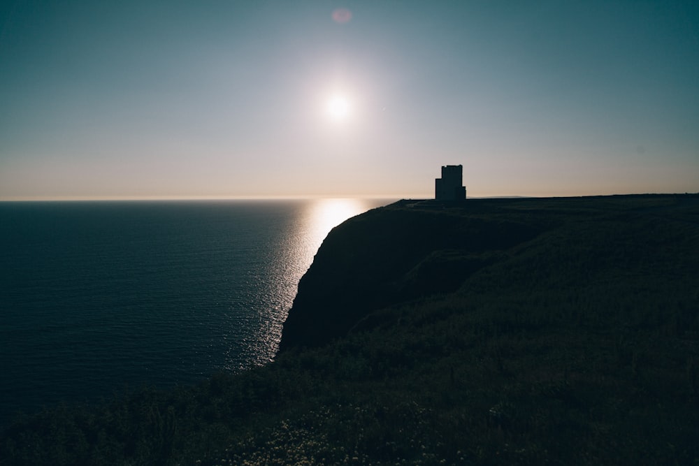 the sun is setting over the ocean on a cliff