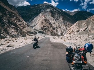 A winding mountain road with two motorbikes parked beside a scenic overlook at sunset.
