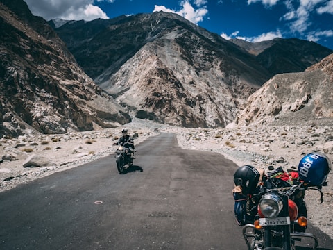 A winding mountain road with two motorbikes parked beside a scenic overlook at sunset.