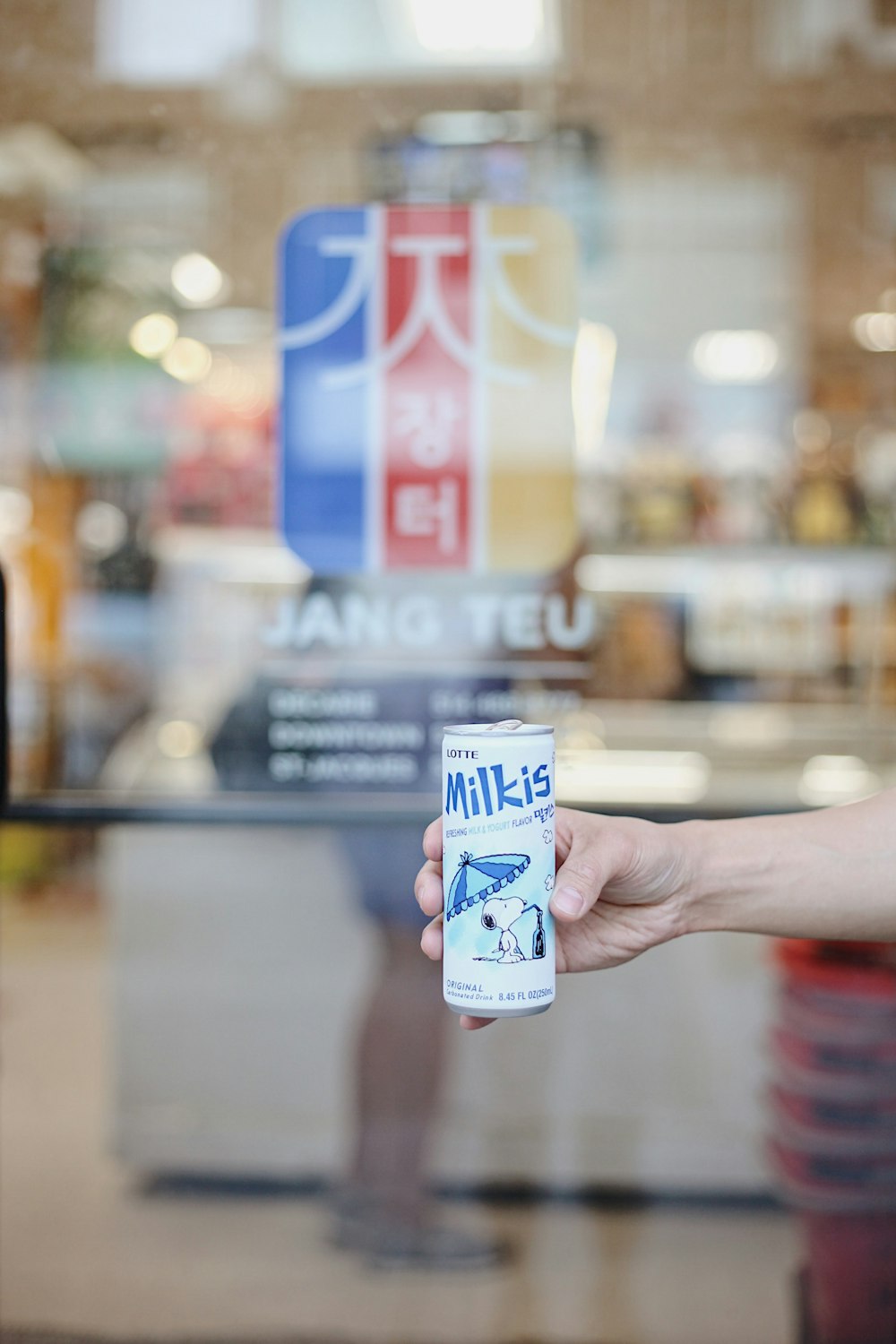 person holding Milkis can besides Jang Teu logo