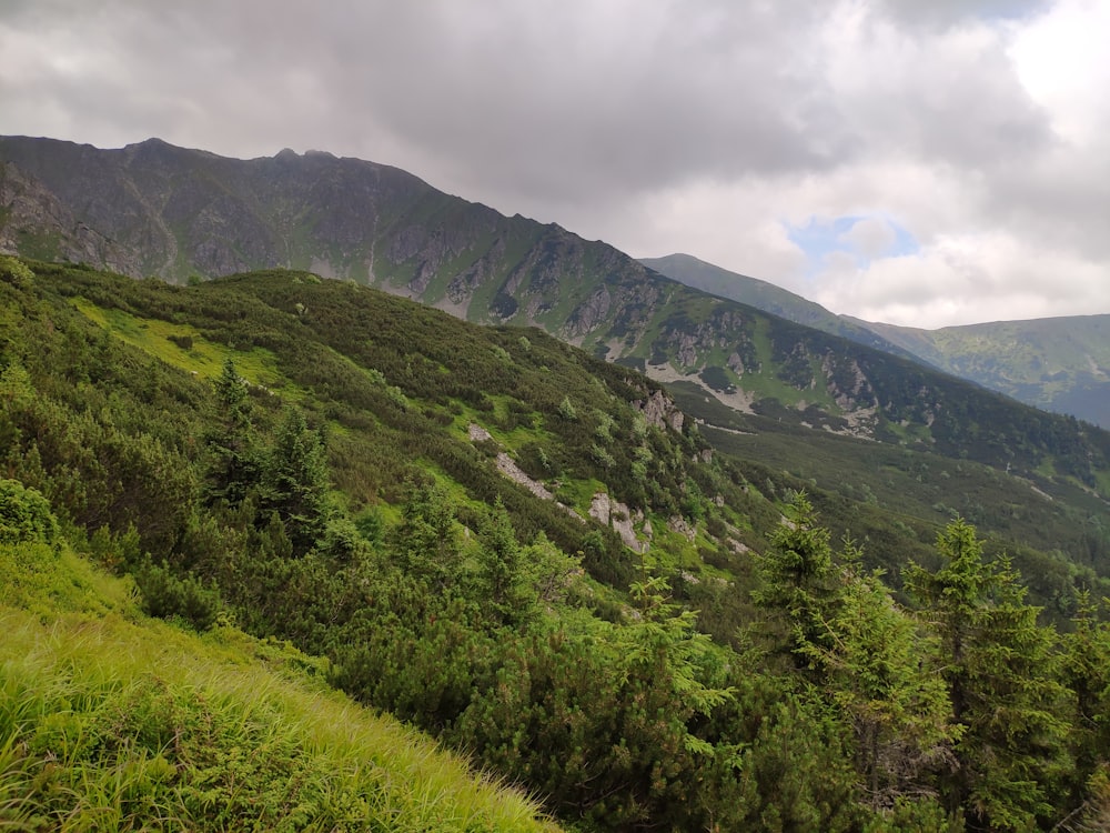 landscape photo of green mountains under by white clouds