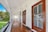 A polished wooden porch lined with white railings and walls, featuring a dark wood front door. There's a metal lantern hanging from the ceiling, and a view of a green lawn and trees is visible in the background.