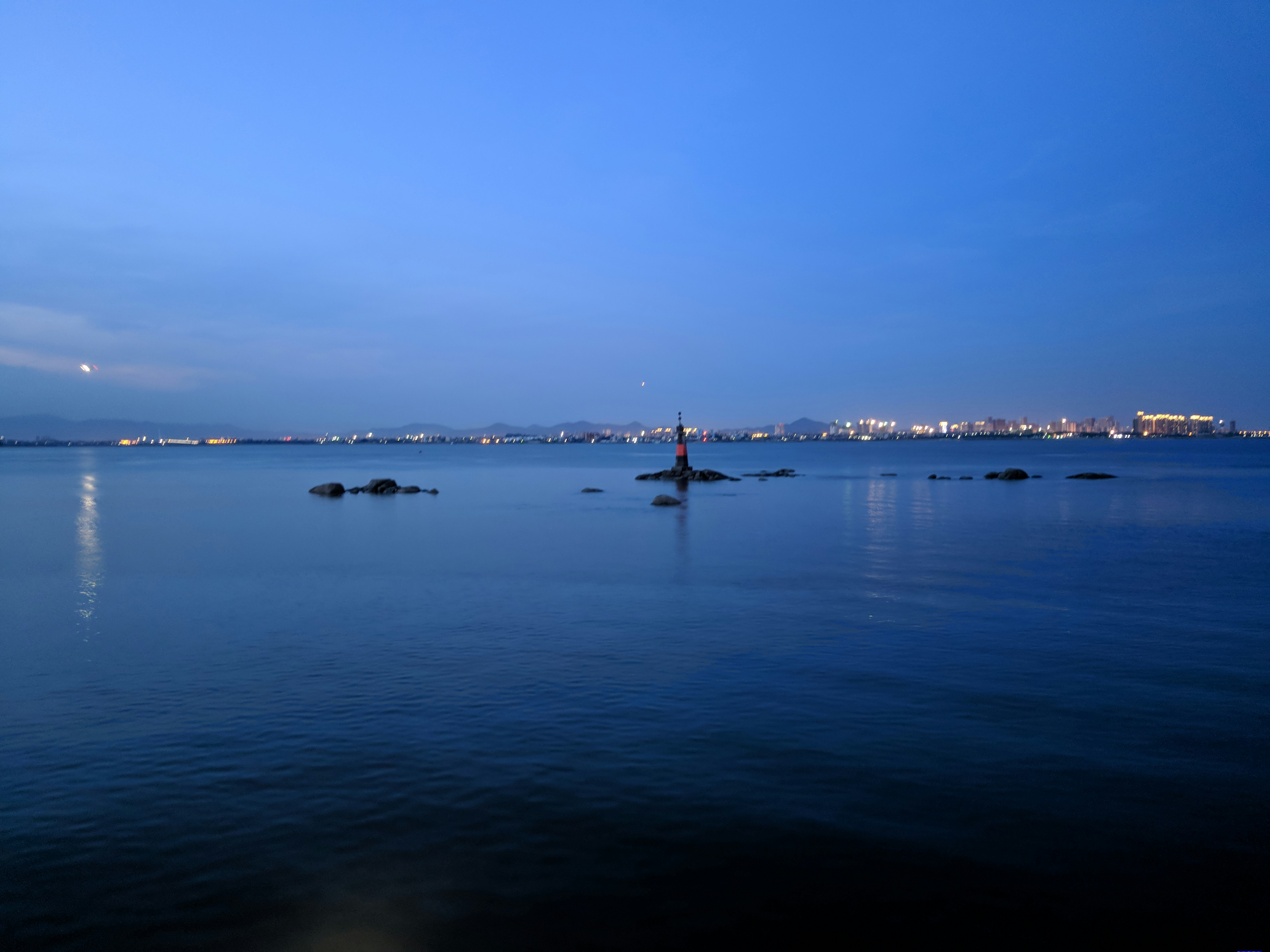 A calm maritime scene with a lighthouse guiding ships at dusk.