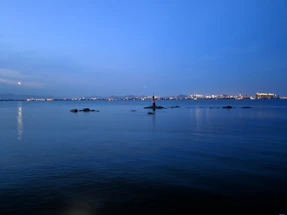 A calm maritime scene with a lighthouse guiding ships at dusk.