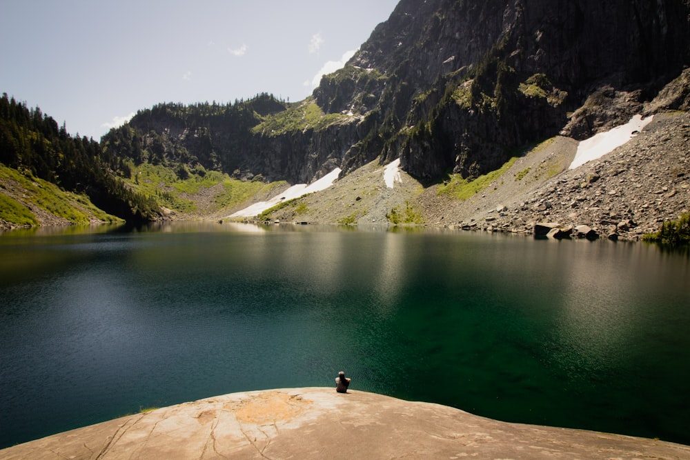 person on rock beside body of water during daytime