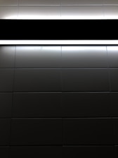A pattern of dark tiles with a light source at the top. The tiles are arranged in a grid and have a glossy finish, reflecting some light. The light creates strong contrasts between the illuminated and darker sections.