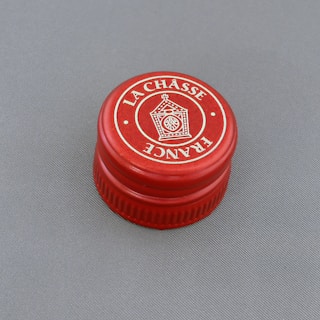 A red bottle cap with 'La Châsse France' printed in white text around a central graphic symbol, displayed against a gray background.