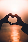 Two hands forming a heart shape silhouette against a warm glowing sky