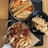 A table with a variety of Korean street food, including tteokbokki with fish cakes and crispy fried toppings, chicken skewers, and a bowl of oden with skewered fish cakes in broth. There are also fried potato wedges and a container of sauce.