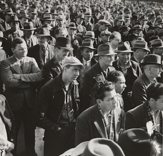 A large group of men stands closely together, most wearing hats and suits, suggesting a formal or organized gathering. The men appear focused and serious.