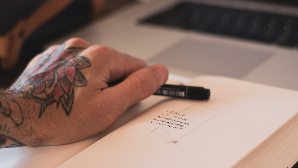 person holding ballpoint pen on opened book