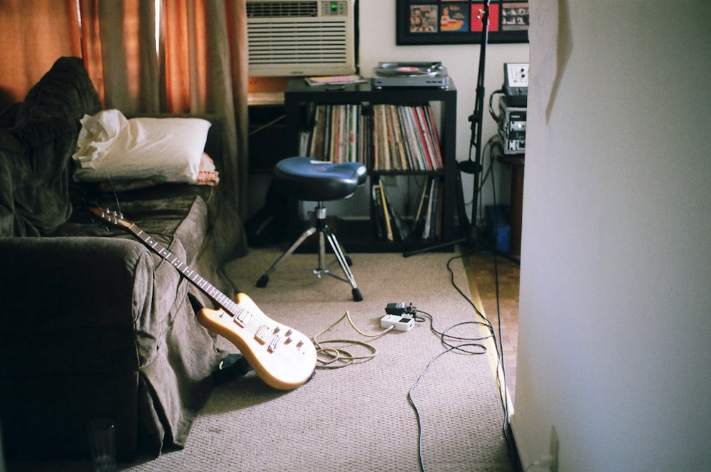 guitarra elétrica marrom apoiada no sofá