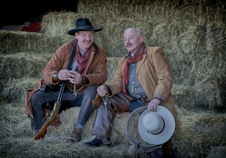 two men in brown coat sitting on hay stack
