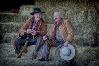 two men in brown coat sitting on hay stack