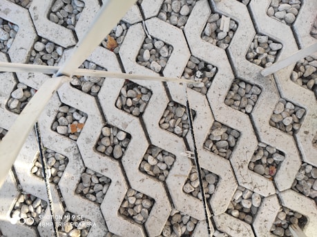 A pattern of interlocking concrete blocks filled with small pebbles, creating a textured surface. Several thin metal rods lay across the blocks diagonally.