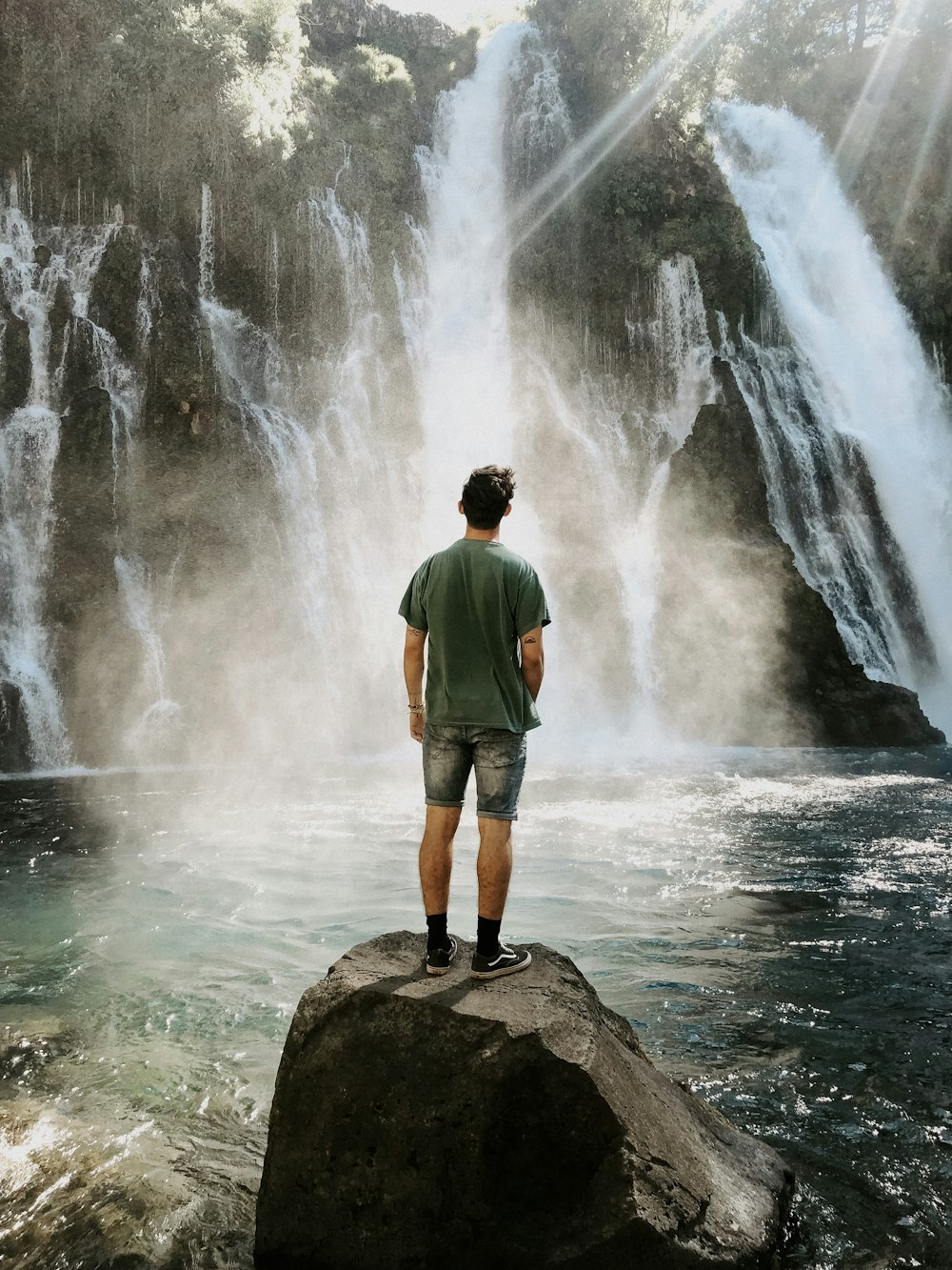 man standing on rock formation facing on waterfalls