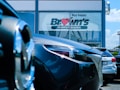 Several cars are parked in front of a dealership with a large window displaying the words 'Buy happy' and 'Brown's Fairfax Mazda'. The focus is on the cars in the foreground, while the dealership building is partially visible in the background.