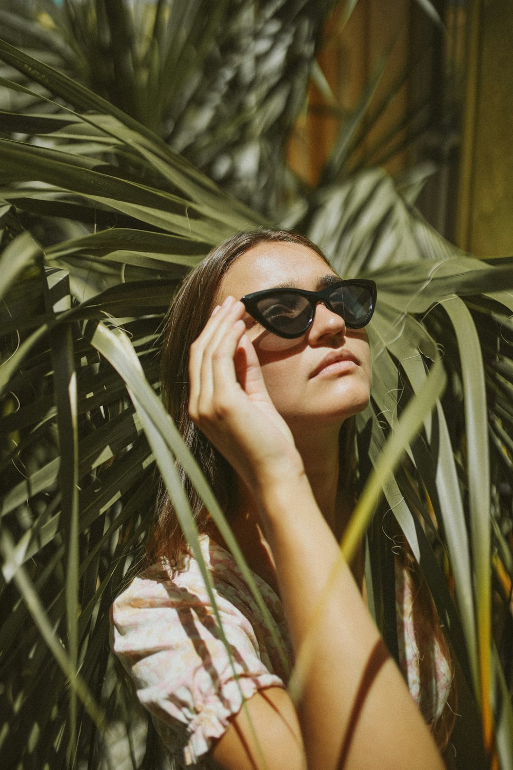 a woman wearing sunglasses standing next to a palm tree