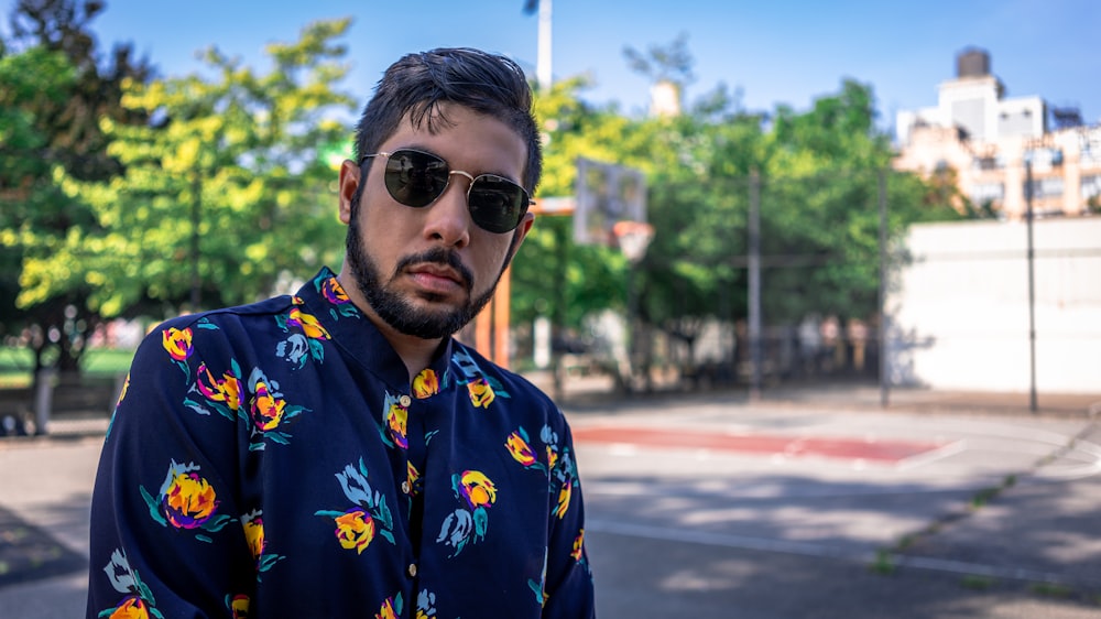 homem em azul amarelo e vermelho botão floral para cima camisa usando óculos escuros pretos