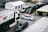 A motorsport paddock filled with support vehicles and race cars. A large white and black truck with 'MP Motorsport' branding is adjacent to a white and blue race car numbered 36. Multiple vans and support tents are visible, indicating a professional racing setup.