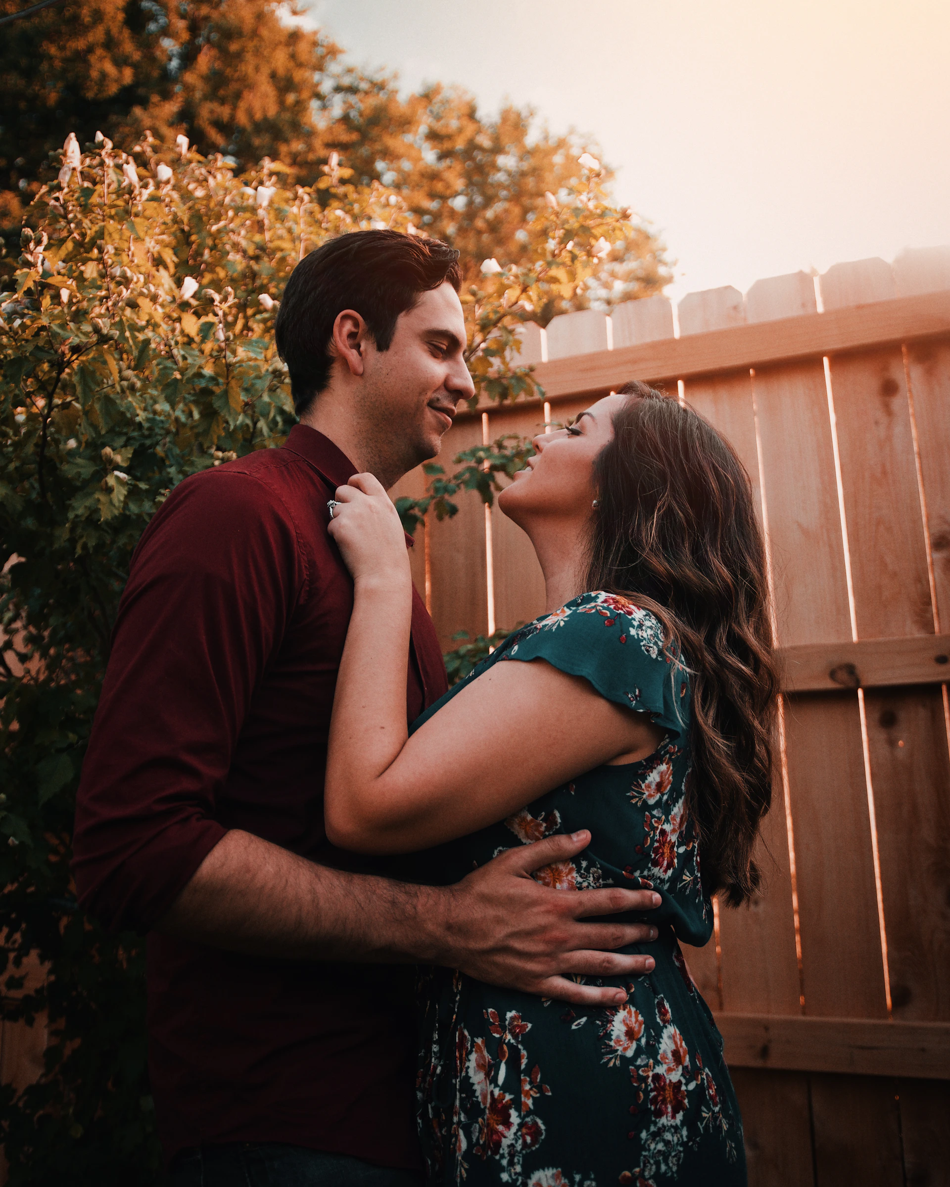 An intimate engagement moment with a couple sharing a quiet laugh against a rustic wooden fence backdrop.