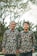 Two individuals stand side by side wearing matching patterned shirts with floral designs. The background features tall trees with a soft blur effect, suggesting an outdoor setting.