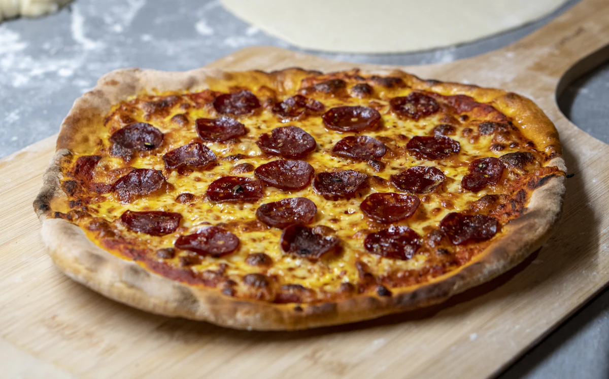 Pepperoni pizza with curled, crisped edges on a dark board