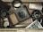 A collection of vintage photography equipment placed in a wooden box. There is a camera, a camera lens, photo slides, a roll of film, a currency note, a lens hood, and a small dial gauge. The items are arranged in an orderly, but casual manner giving a sense of nostalgia.
