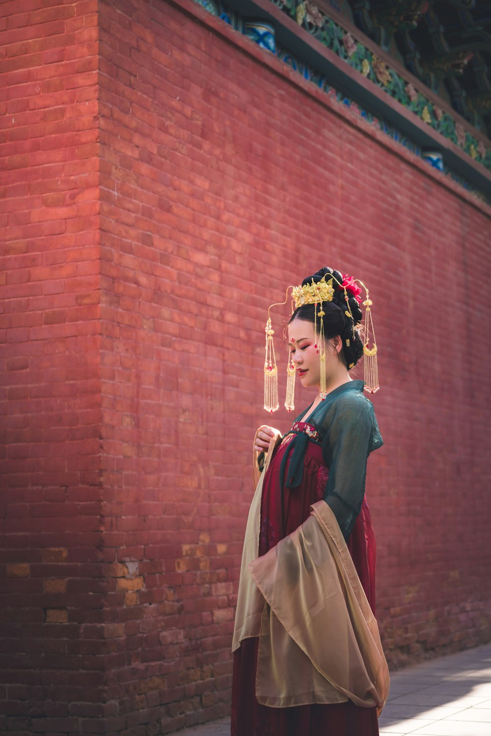 a woman in a traditional chinese dress is standing in front of a brick wall