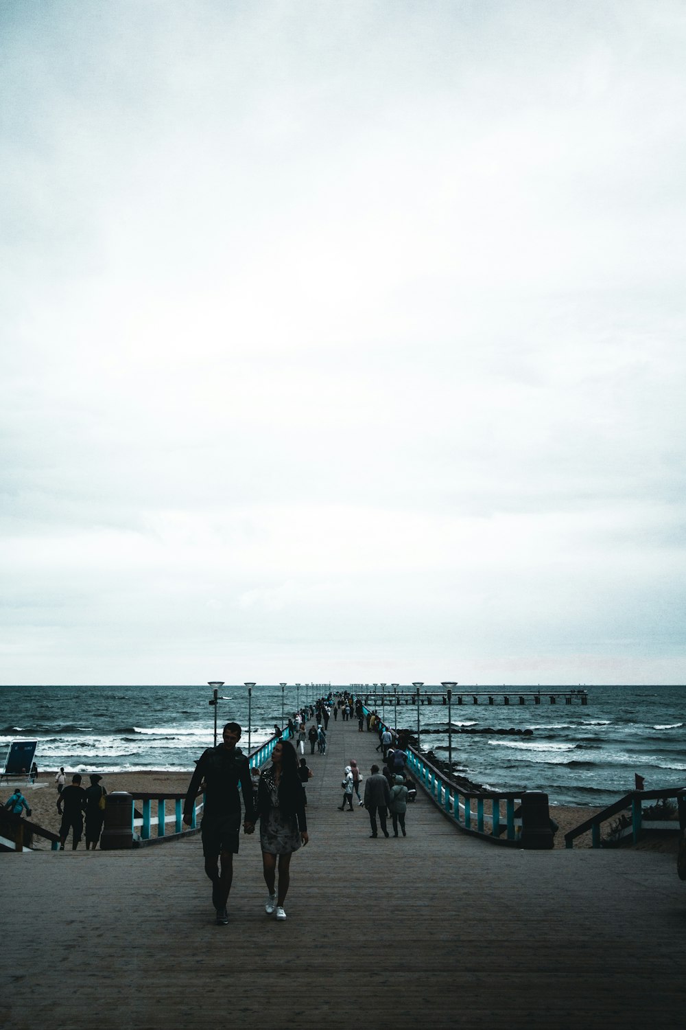 a group of people walking down a pier next to the ocean