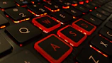 Close-up of a gamer’s hands on a red-backlit mechanical keyboard.