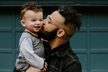man carrying baby boy and kissing on cheek