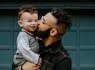 man carrying baby boy and kissing on cheek