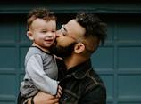 man carrying baby boy and kissing on cheek