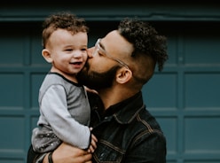 man carrying baby boy and kissing on cheek