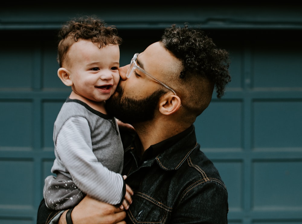 man carrying baby boy and kissing on cheek