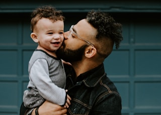 man carrying baby boy and kissing on cheek