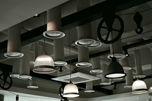 A ceiling with an industrial design featuring various hanging light fixtures and exposed ductwork. The ducts are covered with a textured material, and there are also black metal pulleys and hooks accentuating the design.