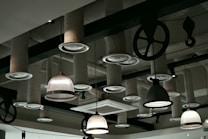 A ceiling with an industrial design featuring various hanging light fixtures and exposed ductwork. The ducts are covered with a textured material, and there are also black metal pulleys and hooks accentuating the design.