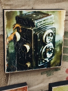 A rustic tintype image of a man holding an old camera, framed with natural wear.