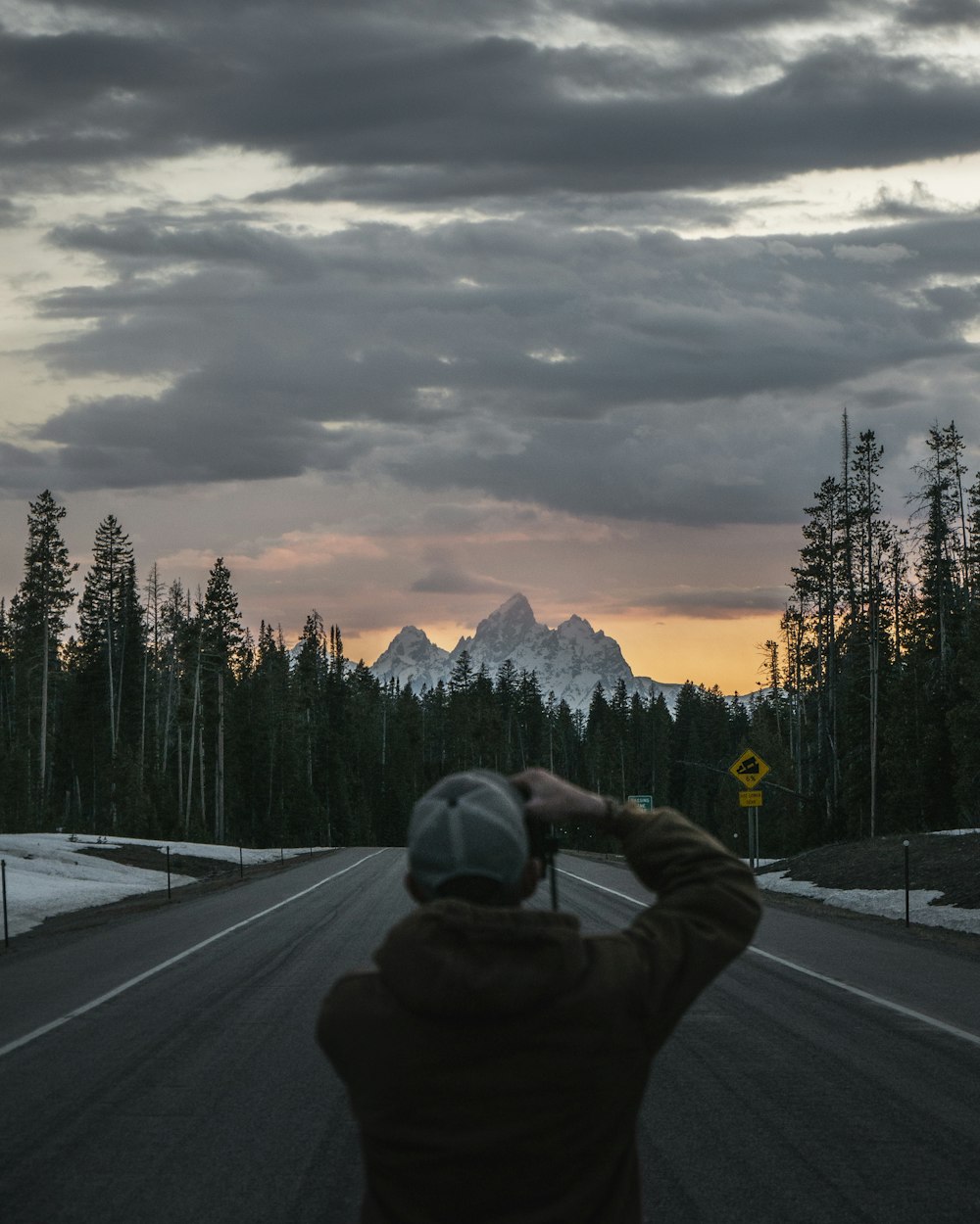 man standing and taking photo of mountain under white skies