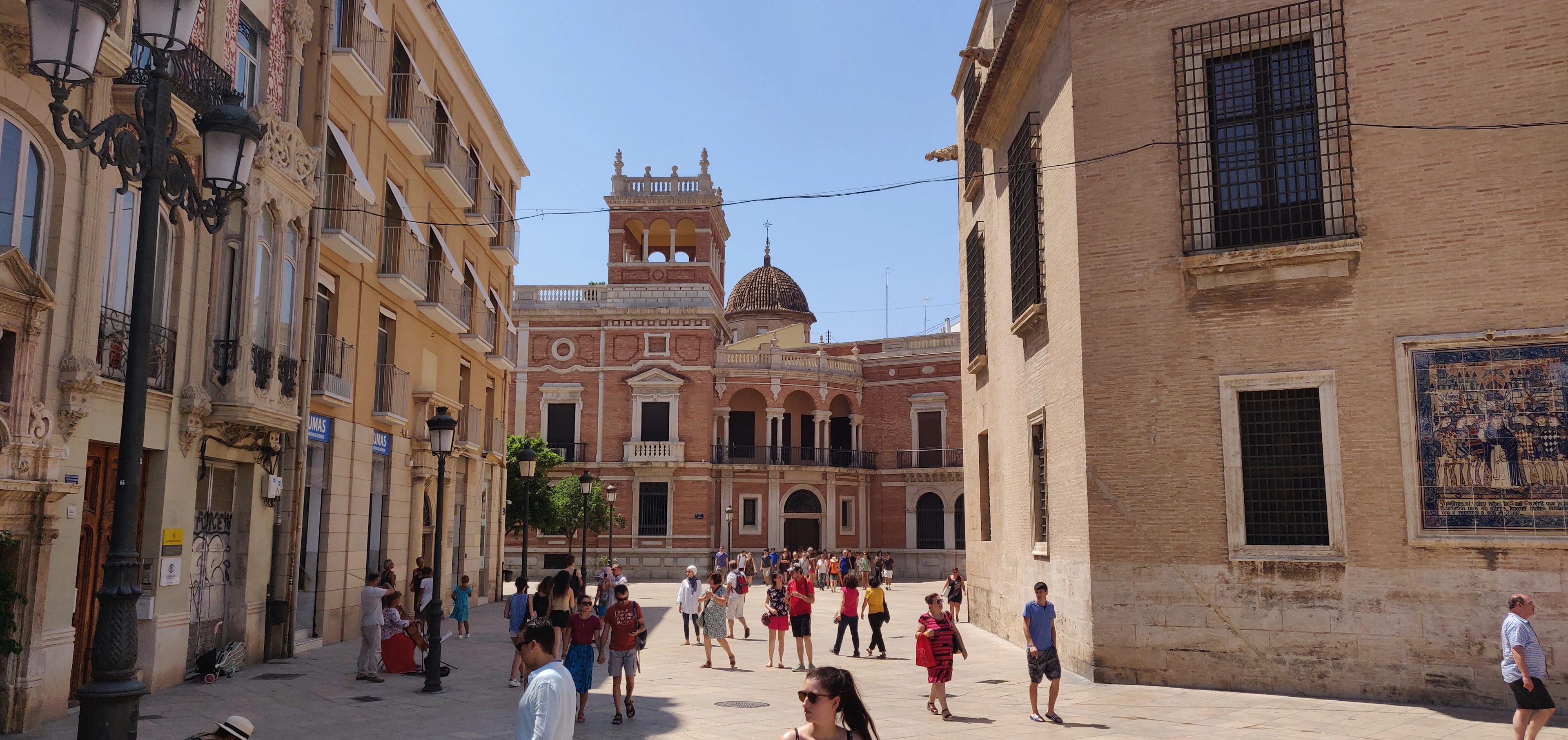 A square in Valencia's old town, ochre and cream facades with a domed church rising behind