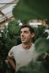Portrait of a friendly trainer standing in a sunlit room with plants, symbolizing growth and calm.