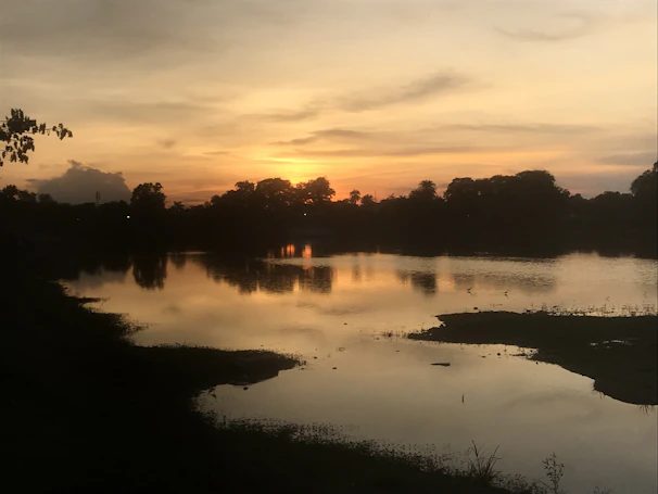 A serene sunset over a calm lake, reflecting warm hues of orange and pink across the water.