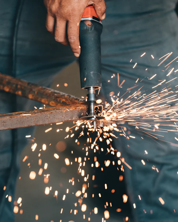 Metal fabrication worker cutting steel frame with angle grinder